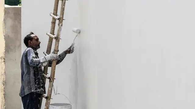 Pintor aplicando pintura vinílica blanca con rodillo en un muro