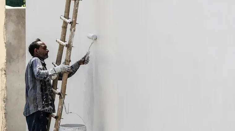 Pintor aplicando pintura vinílica blanca con rodillo en un muro